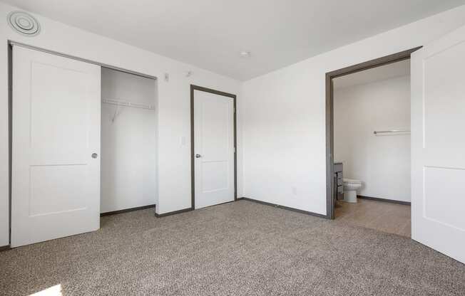 A room with white walls and a carpeted floor with four doors.
