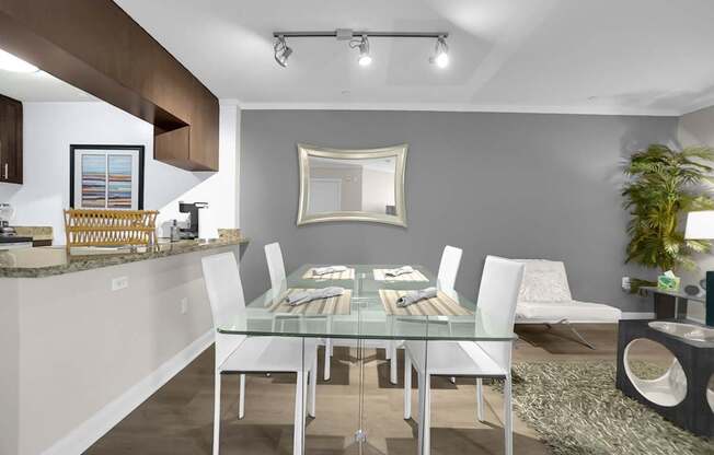 A modern dining room with a glass table and white chairs.
