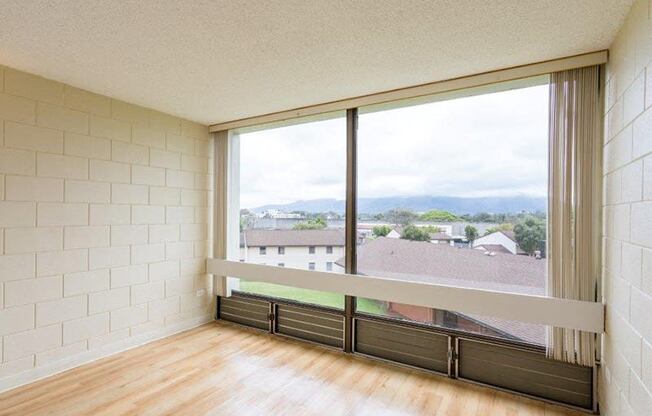 an empty living room with a large window and wood floors at Palms of Kilani Apartments, Wahiawa, 96786