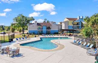 A large outdoor swimming pool surrounded by lounge chairs and trees.