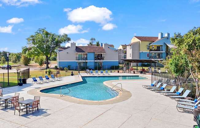 A large outdoor swimming pool surrounded by lounge chairs and trees.