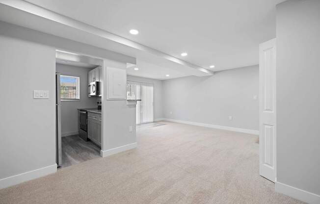 A spacious, empty room with a kitchen area visible through the open door.