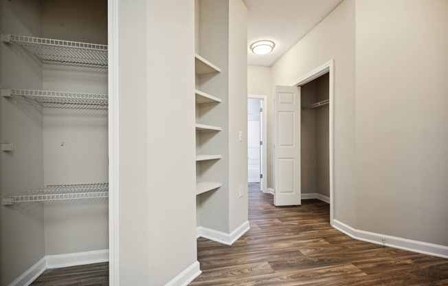 a walk in closet with shelves and a closet door and a door to a hallway