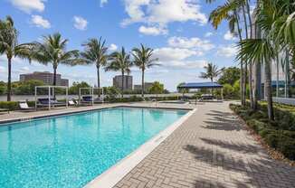 A sparkling swimming pool surrounded by palm trees and brick walkways at Blue Lagoon 7 Apartments in Miami, FL