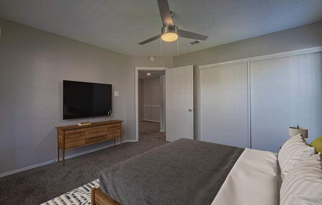 A bedroom with a bed, a television, and a ceiling fan.