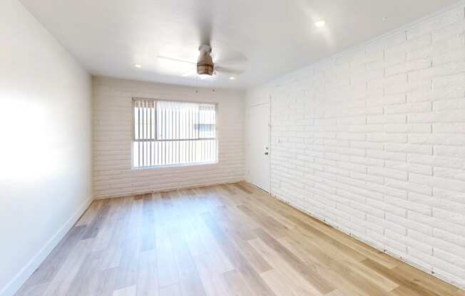 A room with a white ceiling, a window with blinds, and a wooden floor.