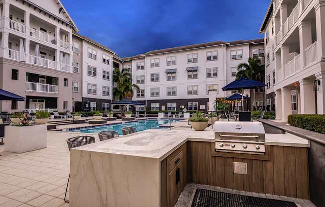 A poolside grill is in front of a pool and apartment buildings.