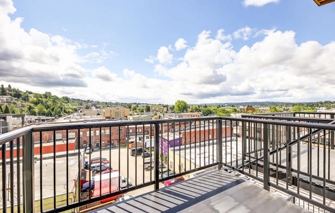 A balcony with a metal railing overlooks a parking lot and buildings.