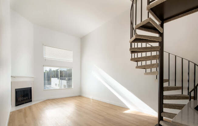 A wooden staircase with a metal railing leads up to a window in a white room.