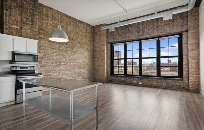 an open kitchen and dining area in an apartment with brick walls and a large windowat Gaar Scott Historic Lofts, Minnesota, 55401