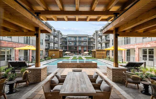 a patio with a wooden table and chairs and a pool in the background