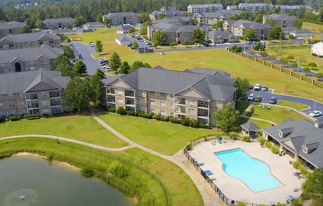 A bird's eye view of a residential area with houses, a swimming pool, and a pond.