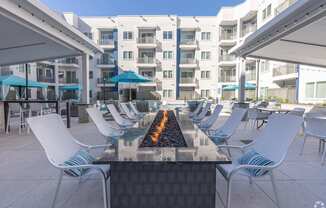 A patio with white chairs and a fire pit in the middle.