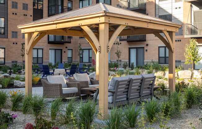 a wooden pavilion with a seating area and a fire pit in front of an apartment building at The Gallery Apartments, Burnsville, MN
