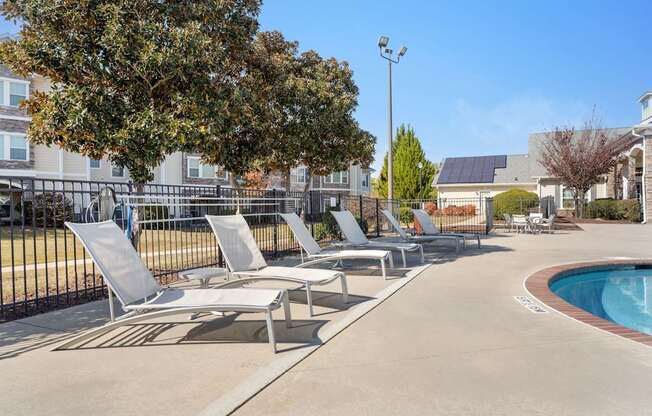 A pool area with sun loungers and a tree.