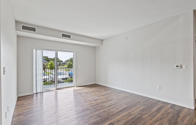 an empty living room with wood flooring and a door to a balcony