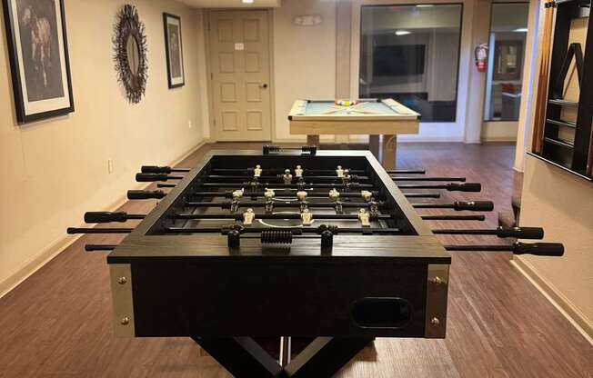 A foosball table in the middle of a room with wood flooring and white walls.