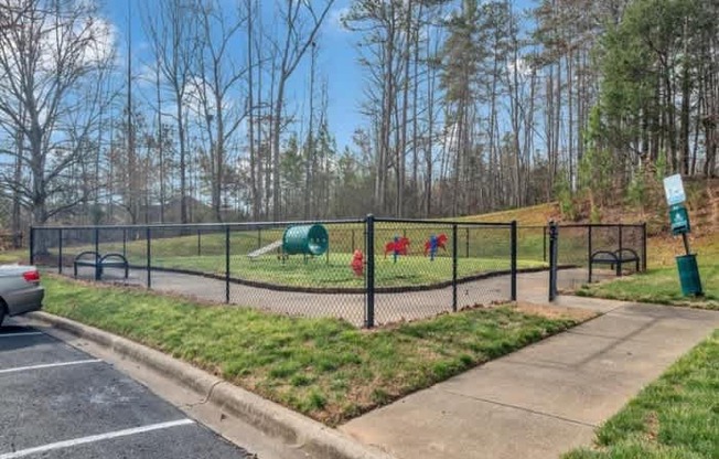 A playground with a green slide and red swings is enclosed by a black fence.