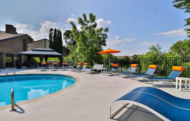 A pool with a blue edge and a white edge with chairs around it.