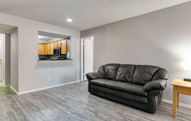 A black leather couch sits in a living room with a wooden table and a painting on the wall.