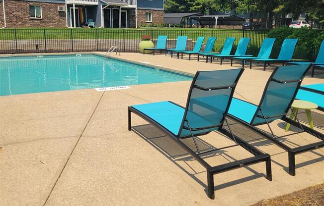 A pool with blue chairs and a bench.