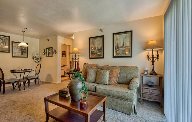 Living room with carpet, windows with blinds, couch, dinner table with chairs, coffee table and wall decor