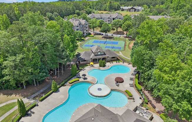 A large resort style pool and tennis court surrounded by trees