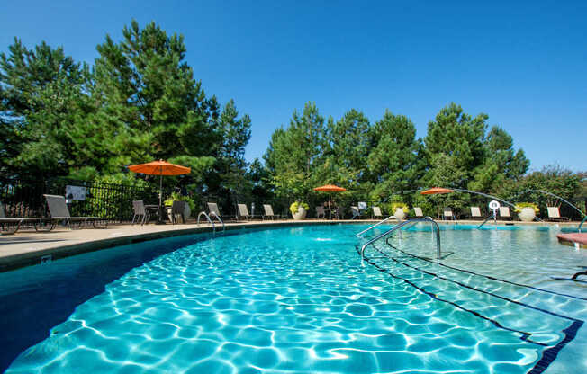 A large swimming pool with a blue tinted water and a sun umbrella.