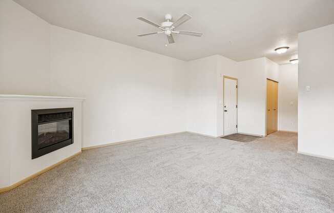 A carpeted living room with a fireplace and a ceiling fan at The Madison Apartments in Olympia, WA