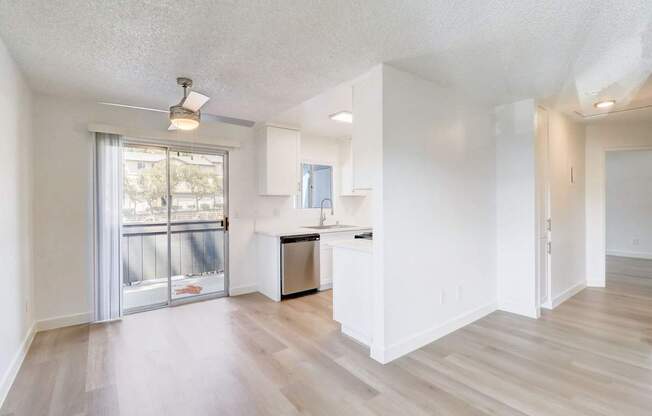 A spacious, empty room with a kitchenette and sliding glass doors leading to a balcony.