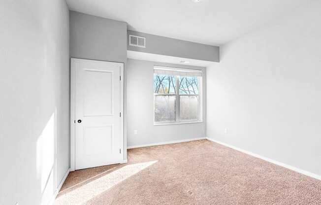 A room with a white door and a window with a view of trees.