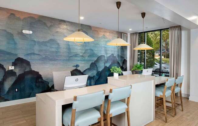 A room with a desk and chairs with a mountain mural on the wall.
