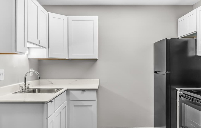 A kitchen with white cabinets and a black refrigerator.