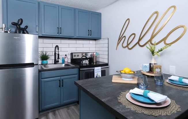 Fusion Las Vegas apartment kitchen with stainless steel electric stove and basin sink, and a large gold sign that reads "hello" in cursive.