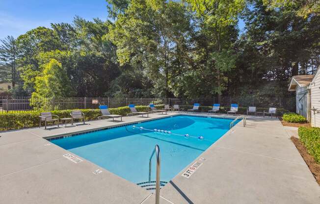 A swimming pool surrounded by trees and chairs.
