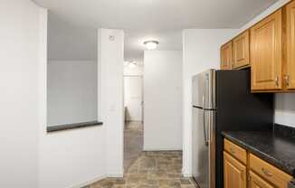 an empty kitchen with a refrigerator and wooden cabinets