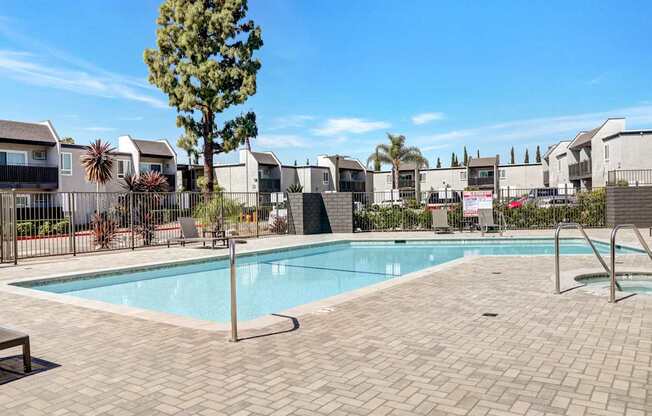 A swimming pool surrounded by a brick patio and a tall tree.