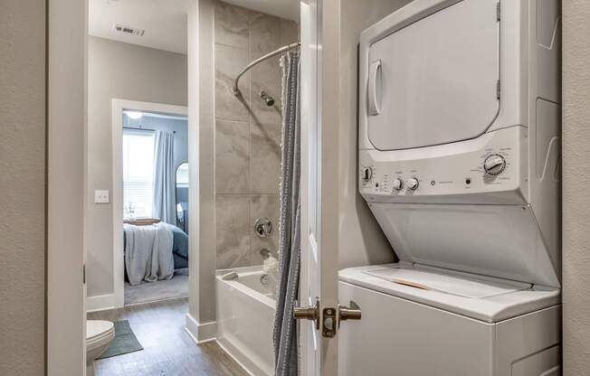 A white washing machine is in a bathroom next to a shower.