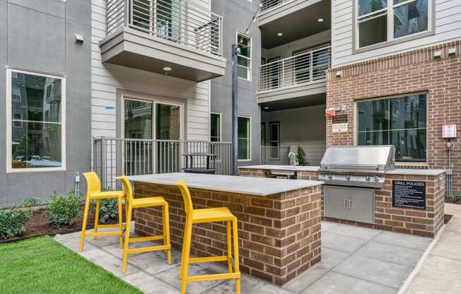 a patio with a bar with yellow chairs and a grill