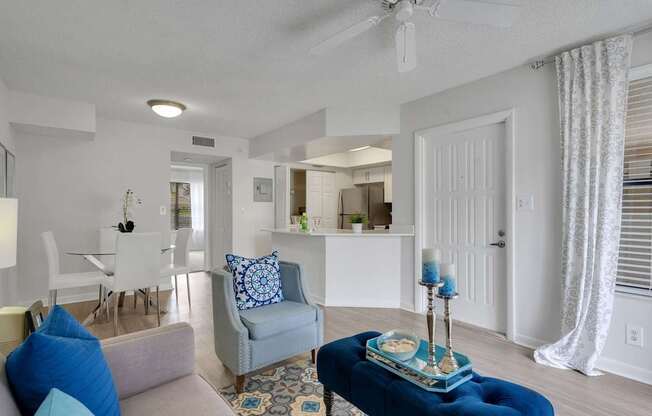 A living room with a grey couch, a blue ottoman, and a white ceiling fan.