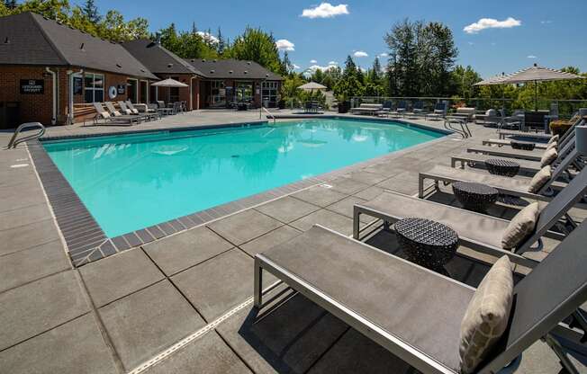 A large outdoor swimming pool surrounded by sun loungers and umbrellas.