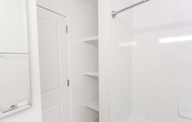 a white bathroom with a white shower door and white shelves