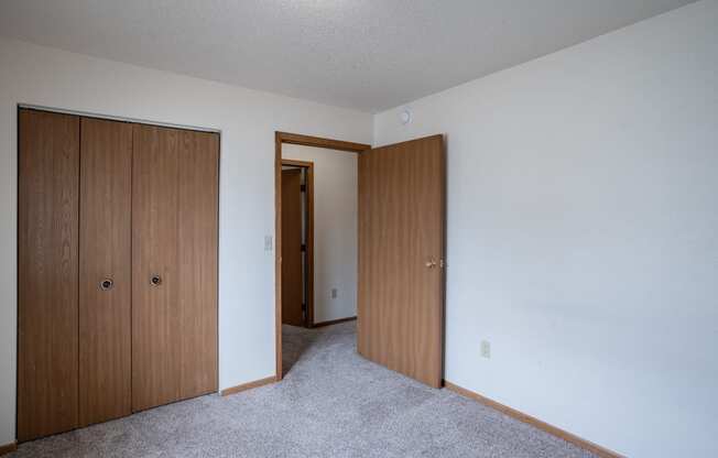 a bedroom with two closet doors and a door to a hallway. Fargo, ND  Prairie Park Apartments