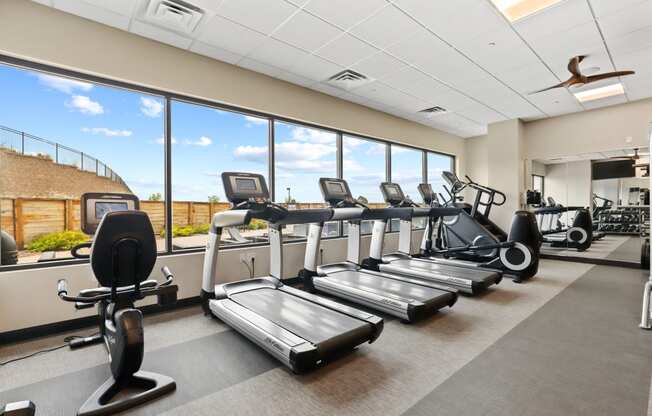 an image of a gym with cardio equipment and windows with a blue sky in the background
