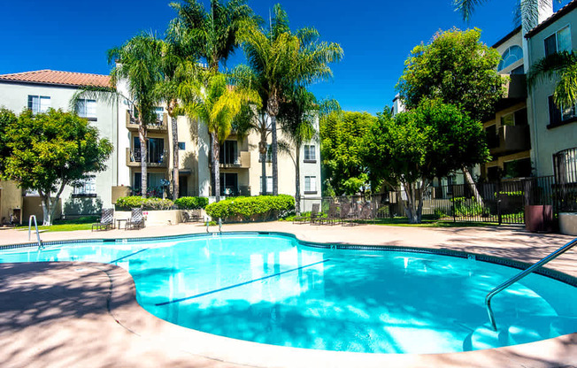 A swimming pool surrounded by palm trees and apartment buildings.