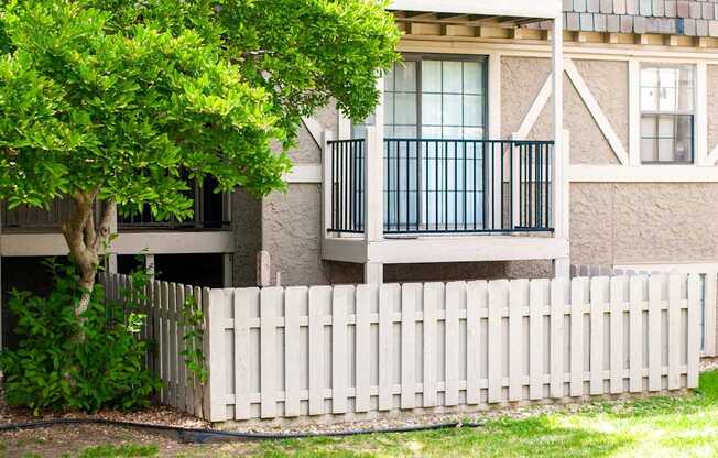 A white picket fence in front of a building with a tree growing over it.
