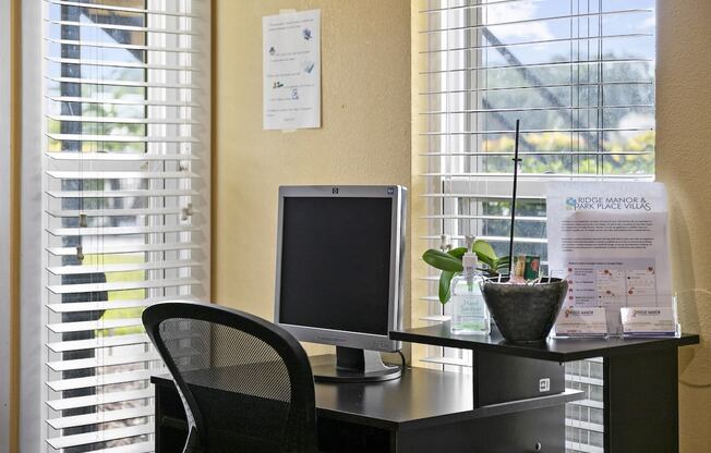 a desk with a computer and a chair in front of a window