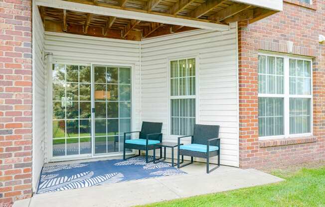 Back patio with two chairs and a rug in front of sliding glass door