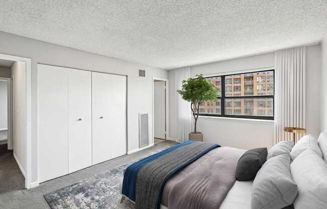 A bedroom with a bed, a chair, and a window overlooking a building.