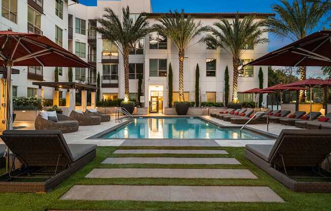 Evening pool deck with illuminated palm trees, cushioned loungers, and a tranquil resort-style atmosphere